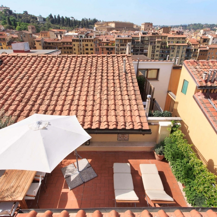 View onto the main terrace with dining table, umbrella, sun beds and gas grill.